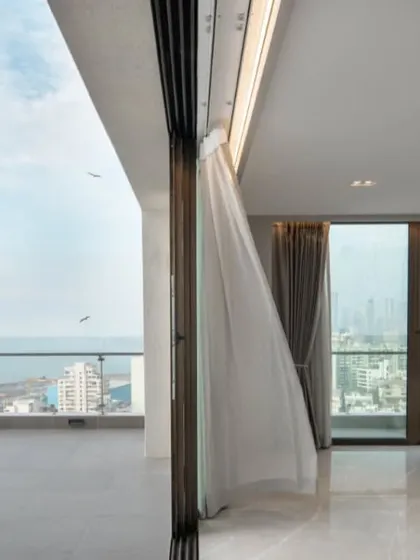 A moment of pause in a sea-facing penthouse. The design prioritizes the view, with floor-to-ceiling glass and an uncluttered layout that creates a seamless transition from the living space to the open sky and water.