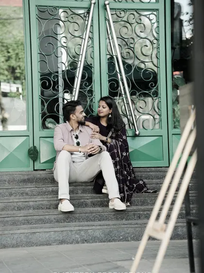 A relaxed couple sits on the steps of a modern building, sharing a conversation, perfect for a casual urban pre-wedding shoot.