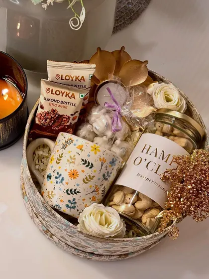 Our "Shubh Diwali" hamper is a cozy and warm gift. It features a printed coffee mug, a jar of premium cashews, a lotus-shaped brass diya, and modak-shaped scented candles.