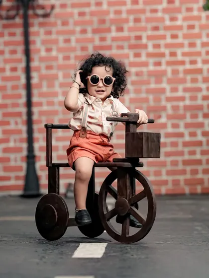A cool and stylish toddler on a wooden tricycle, adjusting his sunglasses like a movie star.