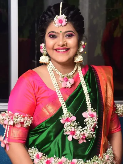 A close-up of the smiling mom-to-be, showing the details of her maang tikka, jhumkas, and layered floral necklace.