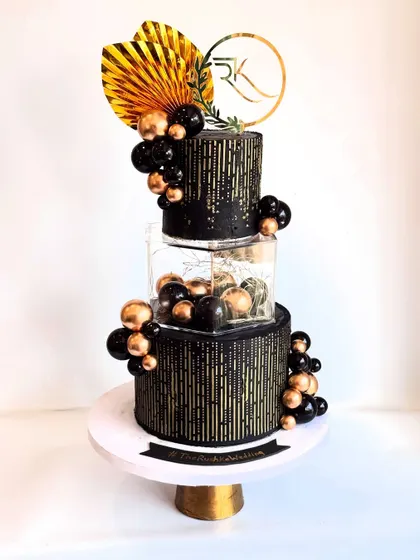 The dramatic silhouette of the three-tier black and gold cake. The spacer tier filled with gold and black spheres adds a unique, floating effect.