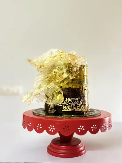 The Belgian Chocolate and dark toffee cake on a vibrant red stand. The contrast of the dark, rich cake with the light wafer paper and gold makes it a true showstopper.