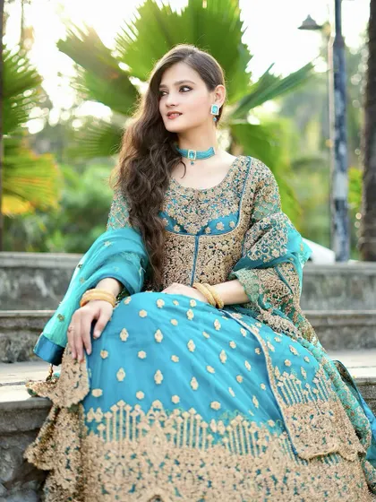 A side profile of the model in the blue Anarkali, seated on steps for a regal feel.