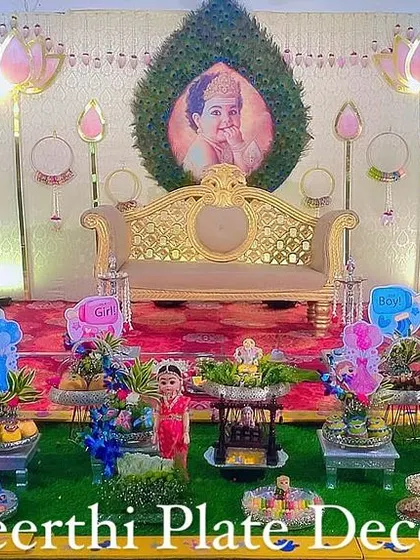 A beautiful baby shower setup with a lotus-themed backdrop and a personalized baby photo. The platter decorations are designed to match the pink and blue color scheme.