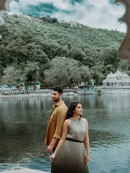 A beautifully framed shot of the couple through white pillars, with the serene lake and hills of Udaipur in the background. This composition adds depth and an artistic touch.