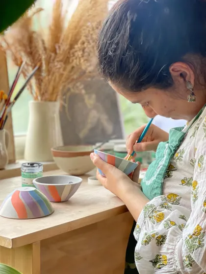 A student carefully paints colorful underglaze onto a set of small bowls, adding a personal and artistic touch to her creations.