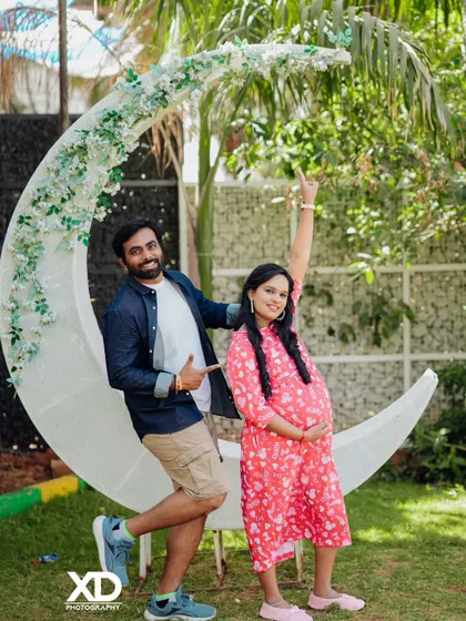 A playful and happy couple's portrait with a large crescent moon prop in a garden.