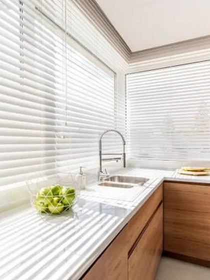 Clean, white Venetian blinds are a perfect choice for this modern kitchen. They are easy to clean, moisture-resistant, and allow for precise control of light over the countertop.