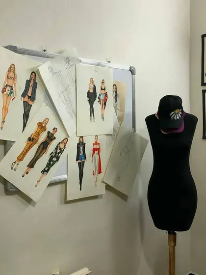 Our classroom walls are often filled with student work, creating an inspiring atmosphere. This image shows a collection of fashion sketches alongside framed illustrations and a mannequin, representing the journey from paper to form.
