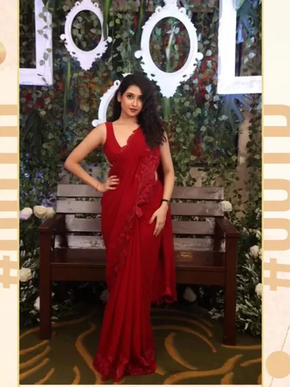 This is a custom-designed red georgette saree-gown for actress Malaika Vasupal. The outfit features delicate floral appliqué on the shoulder and hip, with a pre-draped silhouette that gives the elegance of a saree with the ease of a gown.