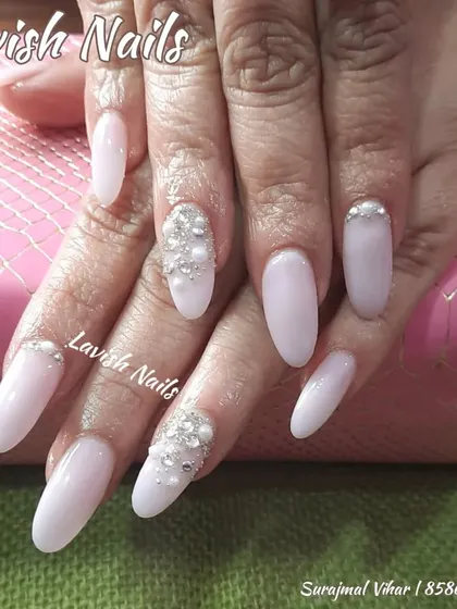 Soft, milky white almond nails are given a touch of luxury with accent nails featuring clusters of pearls and crystals near the cuticle.