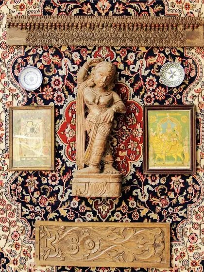 A living testament to the world's rich tapestry of art. This wall combines a Persian carpet with hand-carved wooden sculptures and vintage paintings.