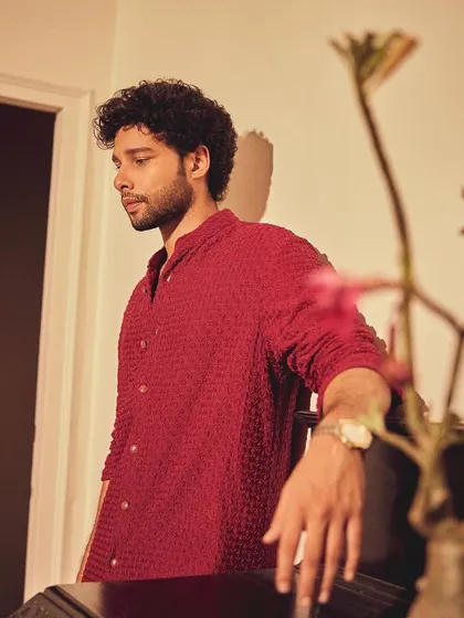 A candid, thoughtful shot of Siddhant in his festive attire. The warm lighting complements the deep red of the kurta perfectly.