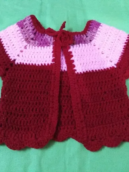 This baby cardigan features a lovely color-block design in maroon, pink, and purple with a simple tie closure at the neck.
