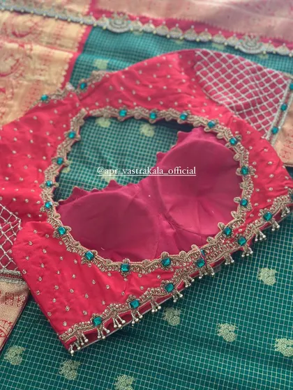 A red blouse with a sheer back panel, adorned with green stones.
