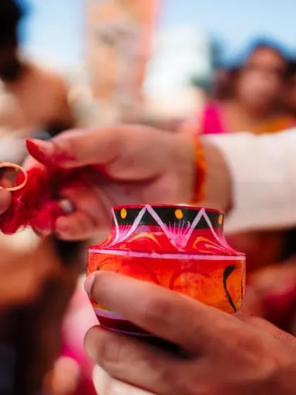A close-up of a wedding ritual, showing a ring being placed in a colorful pot.