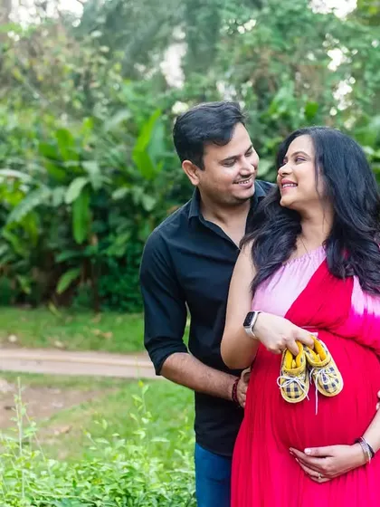 A sweet and simple pose, holding tiny baby shoes over the bump. The vibrant pink dress and the happy expressions make this a cheerful and heartwarming maternity photo.