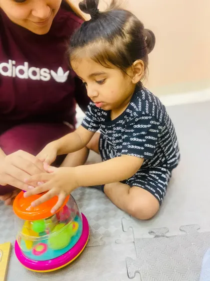 A mother helps her child with a spinning top toy, a simple activity that teaches cause and effect and develops hand strength.