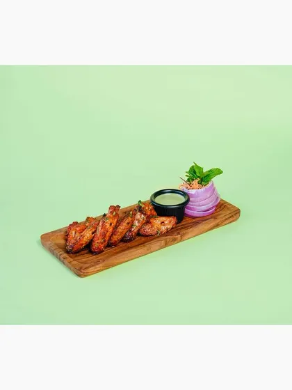 Tandoori chicken wings arranged on a wooden platter with chutney, shot against a pastel green background. The bright, colorful backdrop makes the image pop on a digital menu.