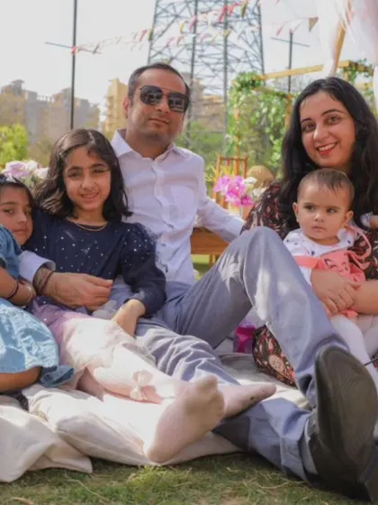 A family portrait taken during a picnic-style birthday party, showing parents and children relaxing together on a mat.