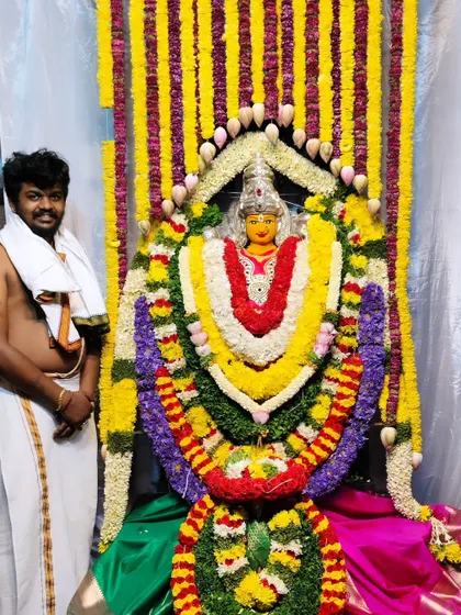 I stand next to my work, a fully decorated deity at the Vasavi Matha Temple, adorned with dense, colorful flower garlands.