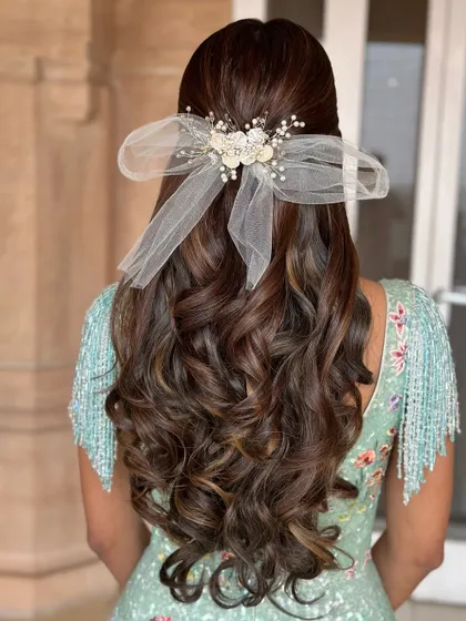 A big hair day with a beautiful half-up style, featuring a large, delicate bow. This look is all about volume and glamour.