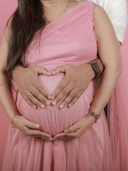 A classic heart-hands pose, with the couple's hands forming a heart shape on the baby bump.