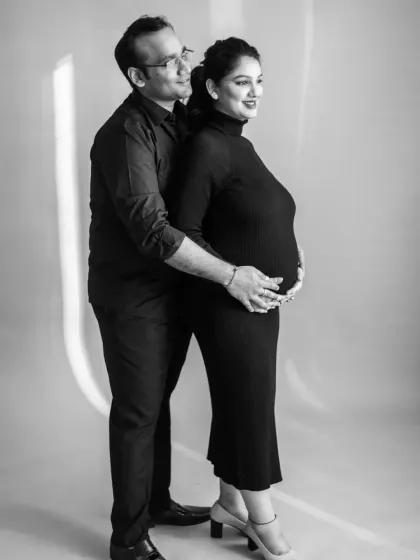 A classic black and white portrait of the couple together. The back-to-front pose creates a sense of protection and intimacy, with their hands joined over the baby bump.