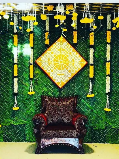 A backdrop featuring a woven green mat, vertical flower garlands, and a central hand-painted kolam art piece. This design blends rustic textures with traditional art for a unique look.