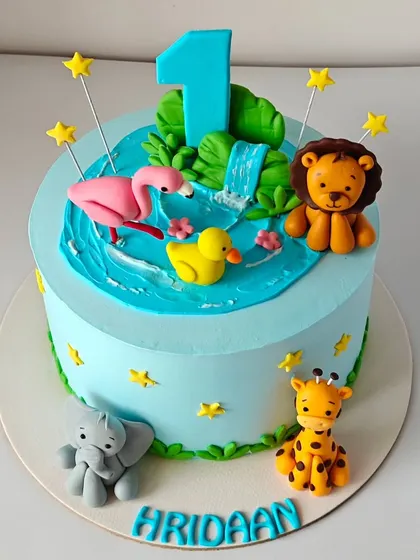 The finished "AI to reality" cake for Hridaan's first birthday. It features a waterfall, a flamingo, and several cute jungle animals, all handcrafted from fondant to bring a digital dream to life.