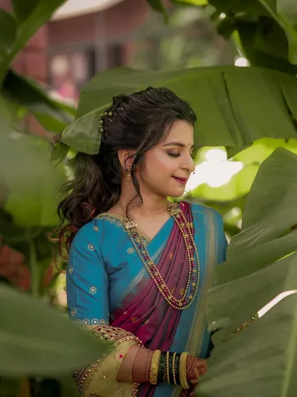 A beautiful bridal portrait, with the bride framed by large banana leaves, her traditional blue and pink saree standing out.