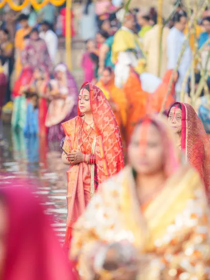A crowd of women in colorful sarees stand in the water for Chhath Puja. The festival is a vibrant display of color, culture, and devotion.
