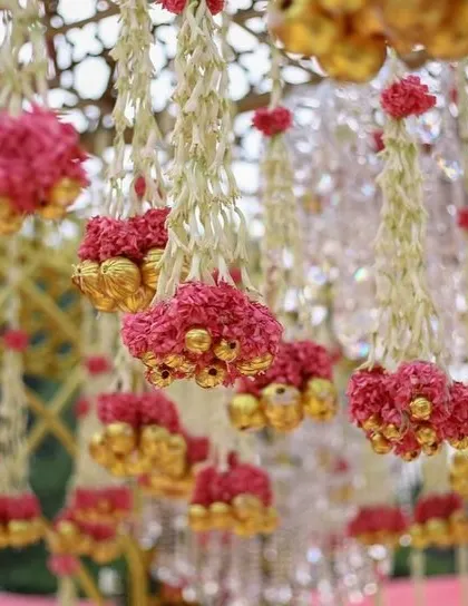 A close-up of the hanging floral details inside a mandap. The decor features strings of jasmine and pink flowers with golden bells.