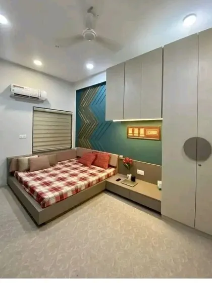 A cozy bedroom design featuring an L-shaped bed, a compact study nook, and a full-height wardrobe. The feature wall with a geometric wooden pattern adds a unique touch.