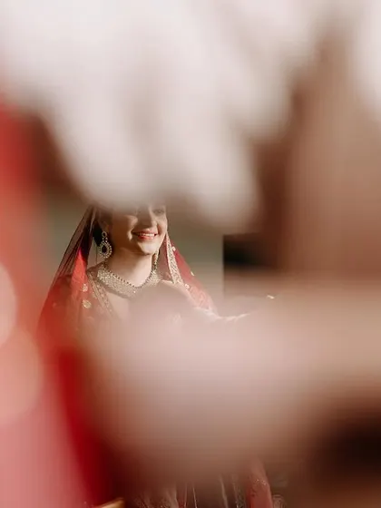 A creative, blurry shot capturing the bride's smile through a red veil, creating an artistic and intimate feel.