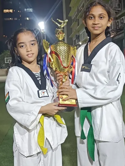 Two students, a yellow belt and a green belt, holding the championship trophy together. This shows that everyone contributes to the team's victory.