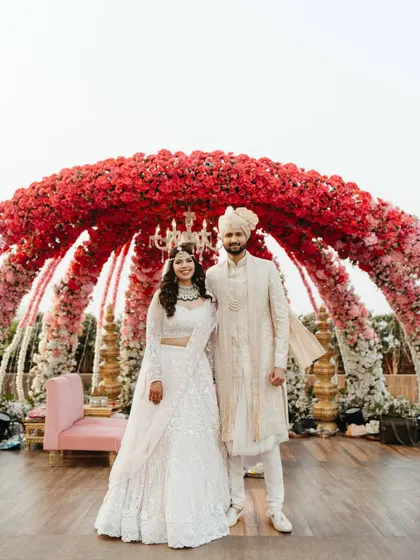 A classic portrait of the couple after their varmala, standing together under the magnificent floral arch. They look serene, happy, and officially united.