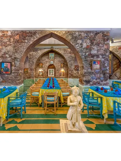 The hotel's restaurant, captured to emphasize its unique character with exposed stone walls, arched ceilings, and brightly colored table settings. This is an example of commercial interior photography for the hospitality sector.