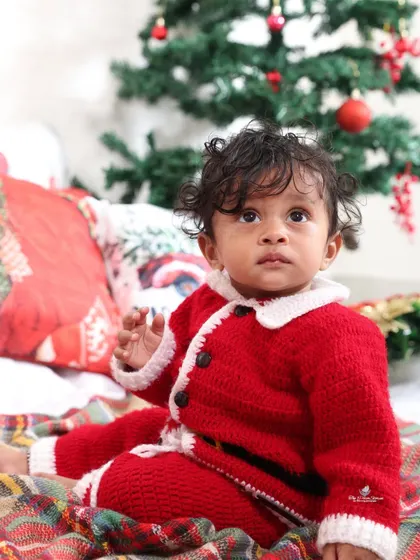 A close-up portrait capturing the wonder in a child's eyes during the holiday season. The soft knit Santa suit adds to the cozy feel.
