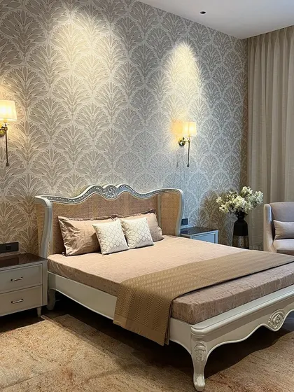 The centerpiece of this room is the bed, featuring a rattan-paneled headboard with intricate carving details. The classic wallpaper and wall sconces add to the room's timeless, quiet luxury.