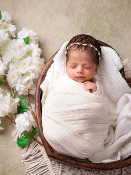 An elegant, all-white setup featuring a heart-shaped wooden bowl and white flowers. This monochromatic style creates a pure and timeless newborn portrait.