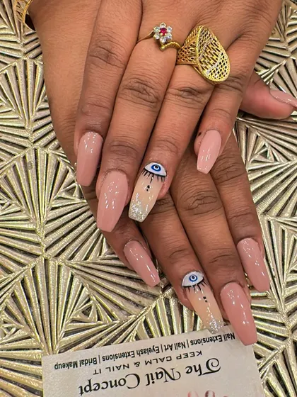 Long, coffin-shaped nude nails with a trendy twist. The accent nails feature hand-painted evil eye designs, with a silver glitter base at the cuticle for extra flair.