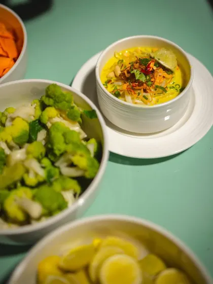A bowl of our signature Khow Suey, surrounded by a colorful array of fresh toppings for customization.