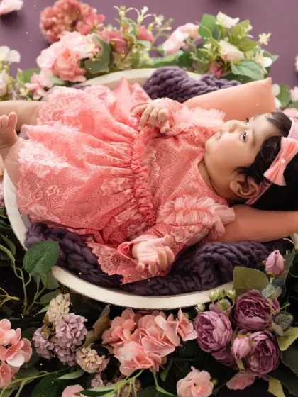 An artistic overhead shot of a baby girl in a pink dress, lying in a bowl surrounded by a sea of flowers.