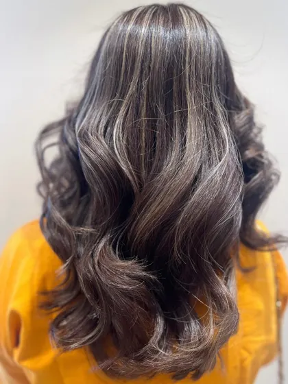 A stunning example of cool-toned ash blonde highlights on a dark base. This look is modern, chic, and styled with beautiful waves to enhance the color contrast.