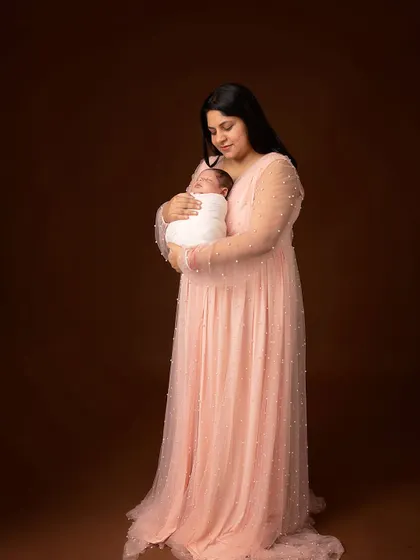 A mother holds her world in her arms. This portrait, with its soft lighting and elegant gown, captures the grace and strength of new motherhood.