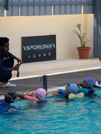 A coach providing instruction to a group of beginners at the pool's edge. This is where we teach fundamental skills like proper kicking technique.