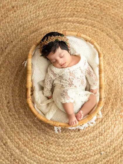 An overhead shot of a sleeping newborn in a lace outfit, nestled in a rustic wicker basket on a jute rug. This highlights my use of natural textures and props.