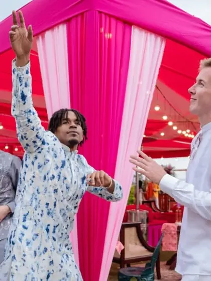 Guests enjoying the daytime festivities at an outdoor wedding event. The vibrant pink tent in the background adds a pop of color to the celebration.